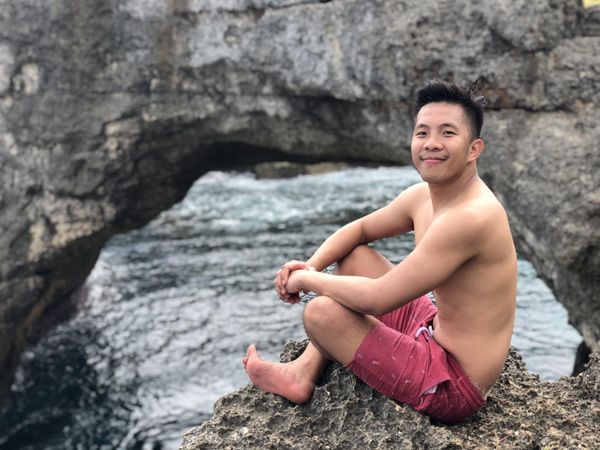 Topless man sitting on a rock at Crystal Bay Nusa Penida beach in Indonesia
