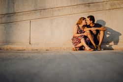 man and woman sitting and kissing at nearby street wall