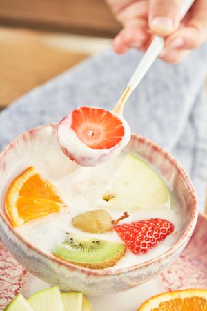 Anonymous person holding spoon with strawberry covered with yogurt