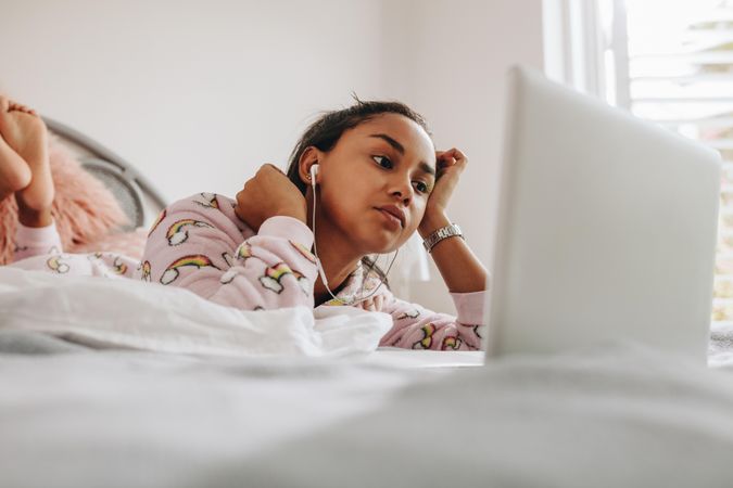 Young woman in bed watching movie on laptop