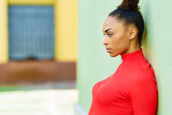 Side view of serious female in casual red dress leaning on wall