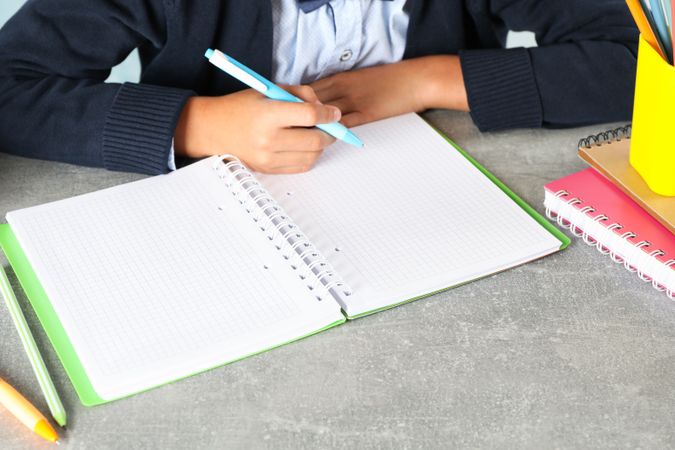 Boy writes in a notebook on grey table, space for text