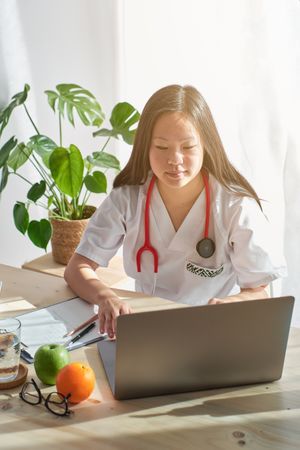 Female doctor working on laptop in examination room lit by sunli