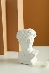 Bust on table with two dried flowers in brown room, vertical composition