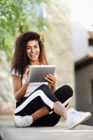 Smiling Arab woman with her digital tablet while sitting outdoors, vertical