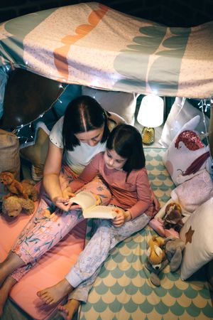 Top view of mother and daughter having a pajama party reading a book