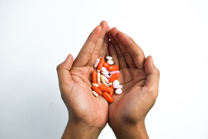 Two hands holding variety of colorful medication and vitamins with plain background