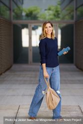 Stylish female standing outside door with thermos and bag 4MG2xx