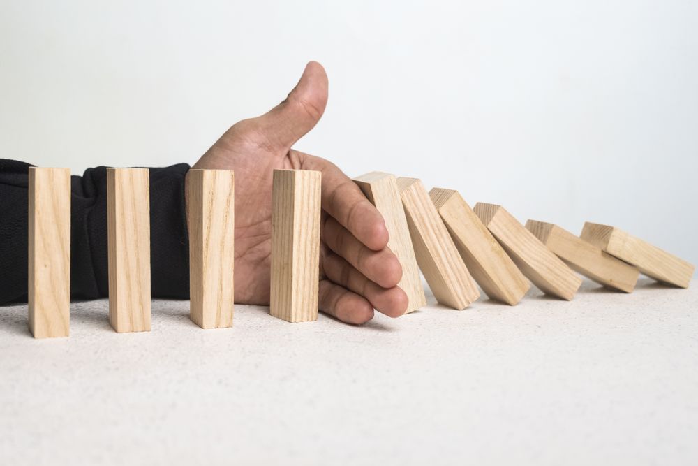 male hand stop falling wooden blocks. domino effect or risk protection strategy concept