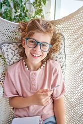 Cheerful boy with notepad lying in knitted hammock