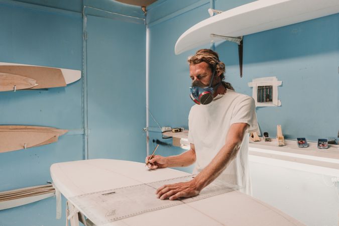 Man in respirator measuring surf board in workshop