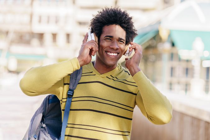 Happy man in yellow shirt listening to music walking outside
