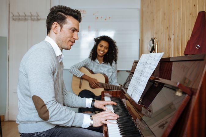 Man playing piano near woman playing guitar in studio