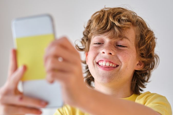Content boy taking selfie on smartphone on light background
