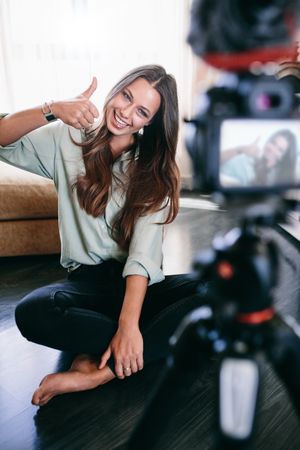 Smiling woman sitting on floor recording content on camera