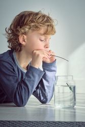 Pensive boy putting fishing rod in glass jar of water