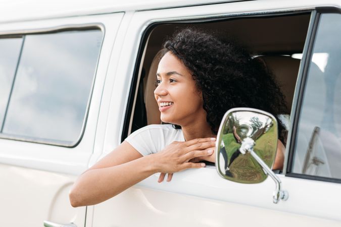 Happy woman with curly hair looking out of a car window looking back
