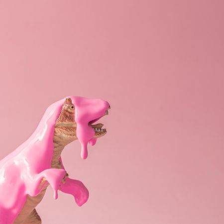 Toy dinosaur on pink background with pink paint dripping on its head