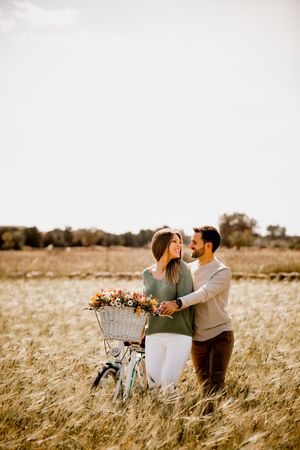 Sincere lovers posing by bicycle on rye field