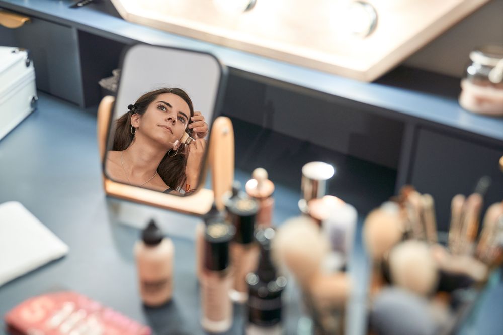 Faceless visagiste applying makeup on woman reflecting in mirror