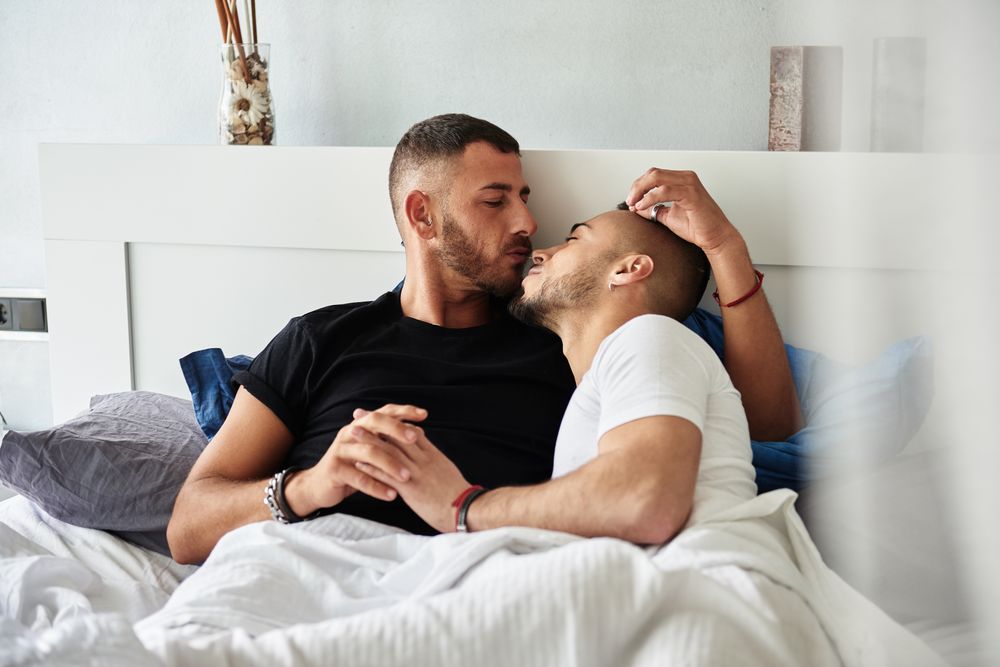 Smiling gay couple hugging and kissing on bed