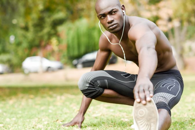 Male warming up legs with shirt off listening to music on headphones