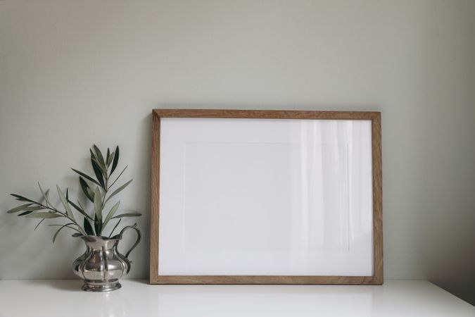 Empty horizontal wooden picture frame mockup with olive tree branches in silver jug
