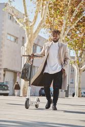 Black male walking with scooter on street