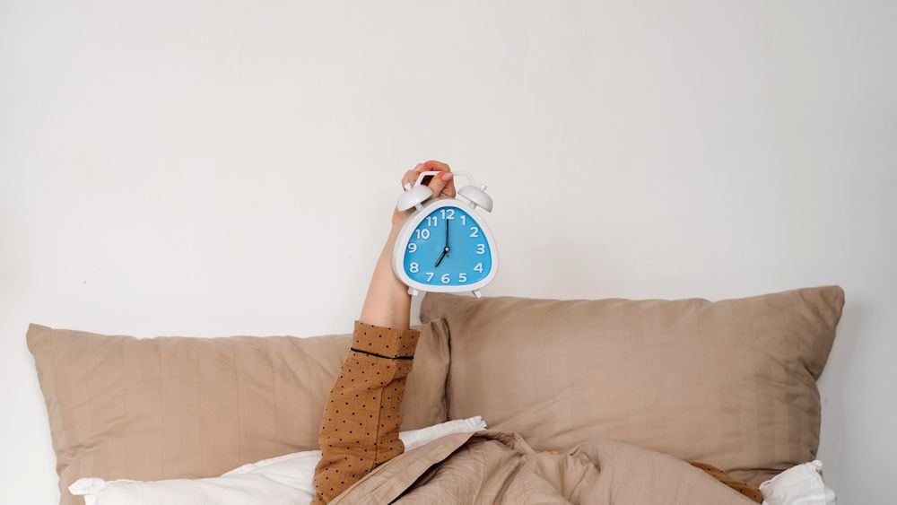 Hand holding alarm clock in bed