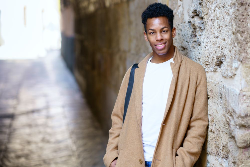 Black male in camel coat leaning on wall in archway