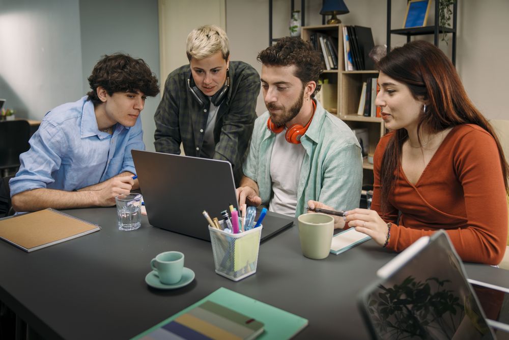 Group of diverse young students collaborating on a project with a laptop in a modern office