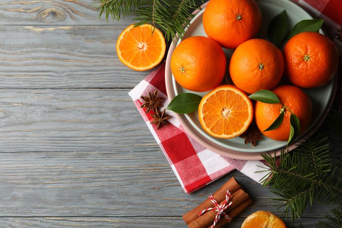 Plates with mandarins, pine branches, napkin and cinnamon on wooden background