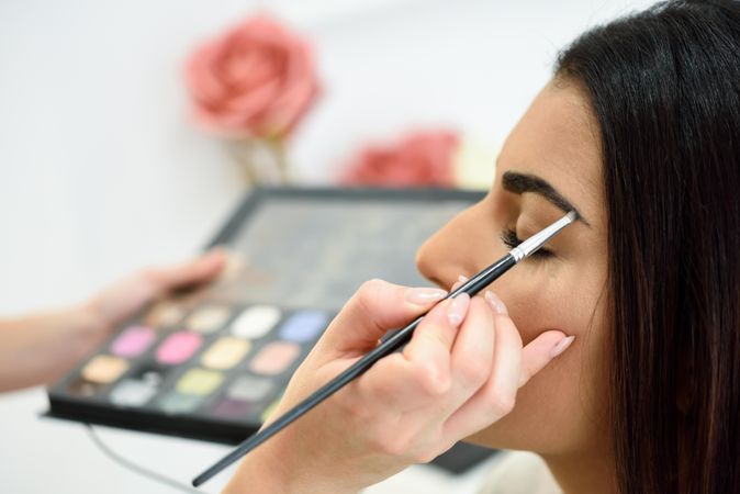 Brush applying make up to woman’s eyes from palette