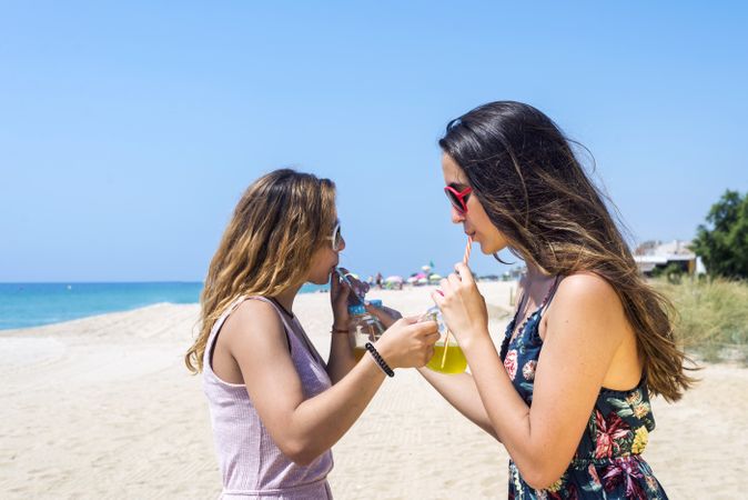 Two female friends on the beach sipping drinks