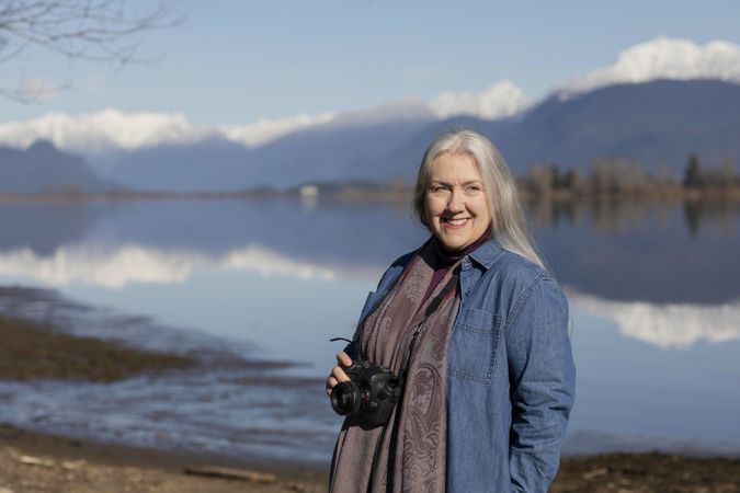 Smiling female photographer stands by a mountain lake