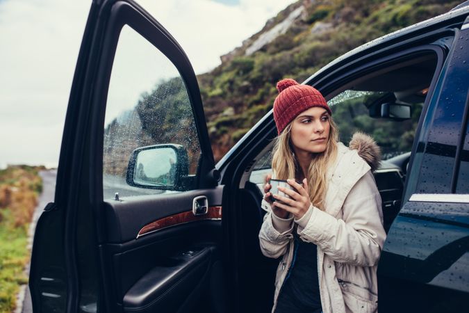 Young woman standing by car with cup of coffee
