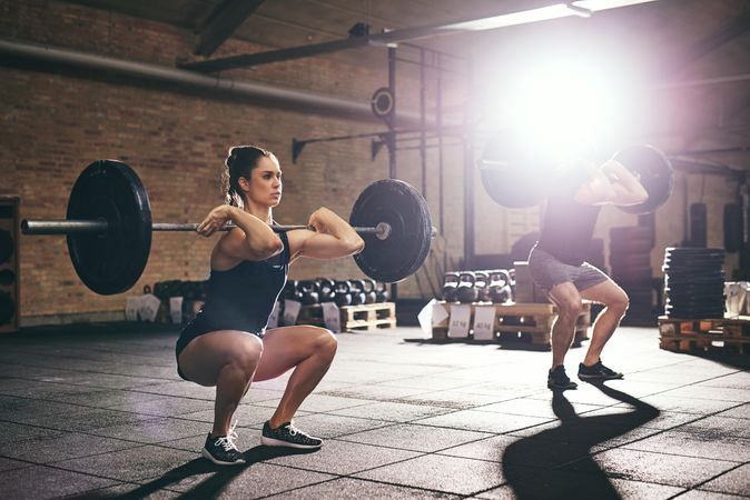 Woman and man holding barbell on shoulders as they weight lift