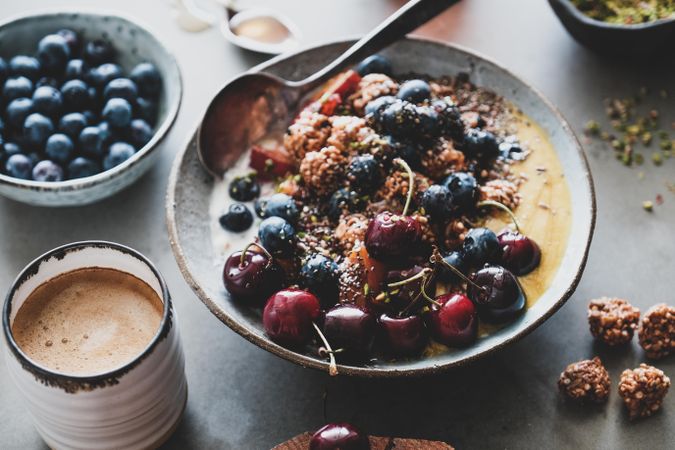 Oat granola yogurt bowl with cherries, blueberries, honey, nuts, coffee