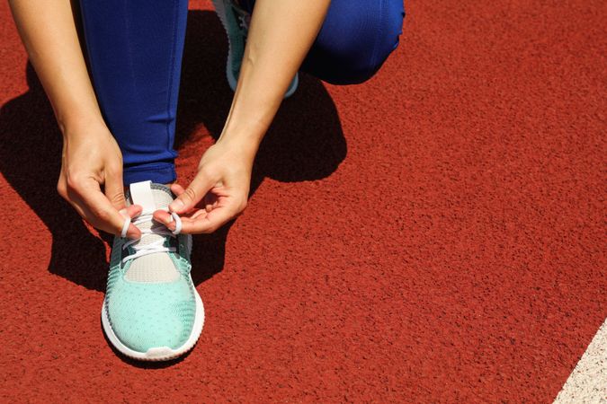 Girl tying shoelaces on red athletic running track, close up