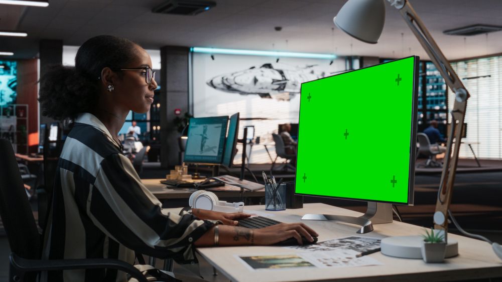 Portrait of Creative Black Female Sitting at a Desk Using Desktop Computer with Mock-up Green Screen.