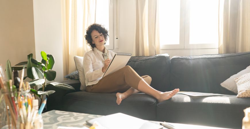 Woman writing on paper on sofa in room