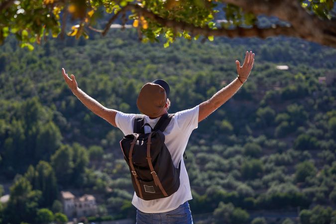 Male traveler with backpack standing in highlands and raising ar