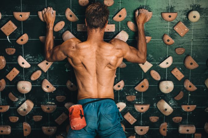 Muscular man climbing wall at indoor wall climbing center