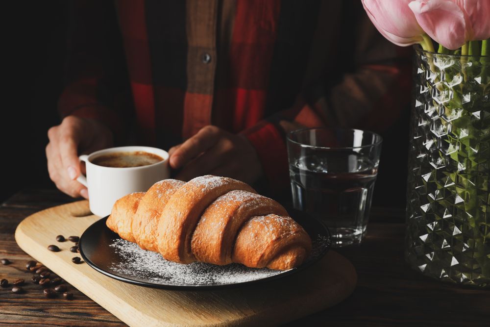Side view of pastry with person reaching for coffee