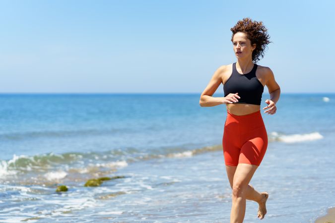 Focused young woman in sportswear running on seashore