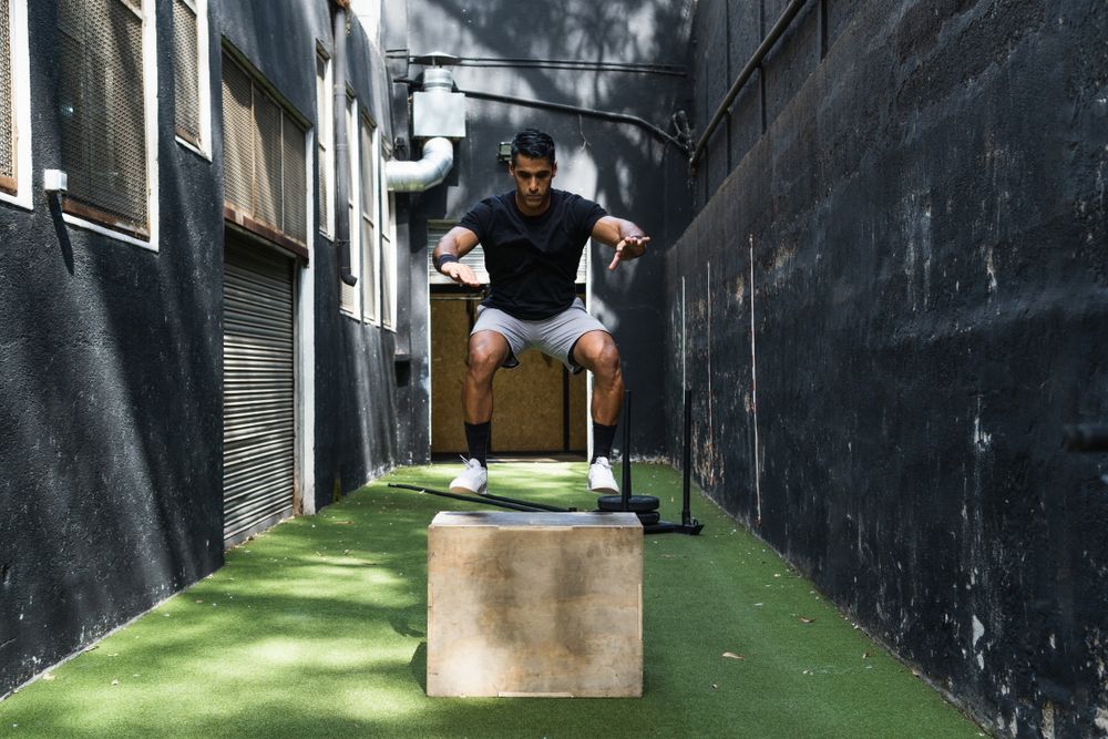 Concentrated athlete jumping on wooden box