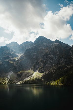 Green and brown mountains beside lake under clouds and blue sky