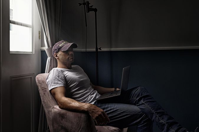 Side view of man sitting on armchair with a laptop