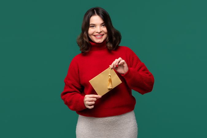 Smiling woman in red sweater holding golden envelope with tassel
