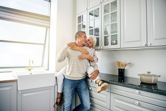 Woman sitting on kitchen counter holding her husband from behind